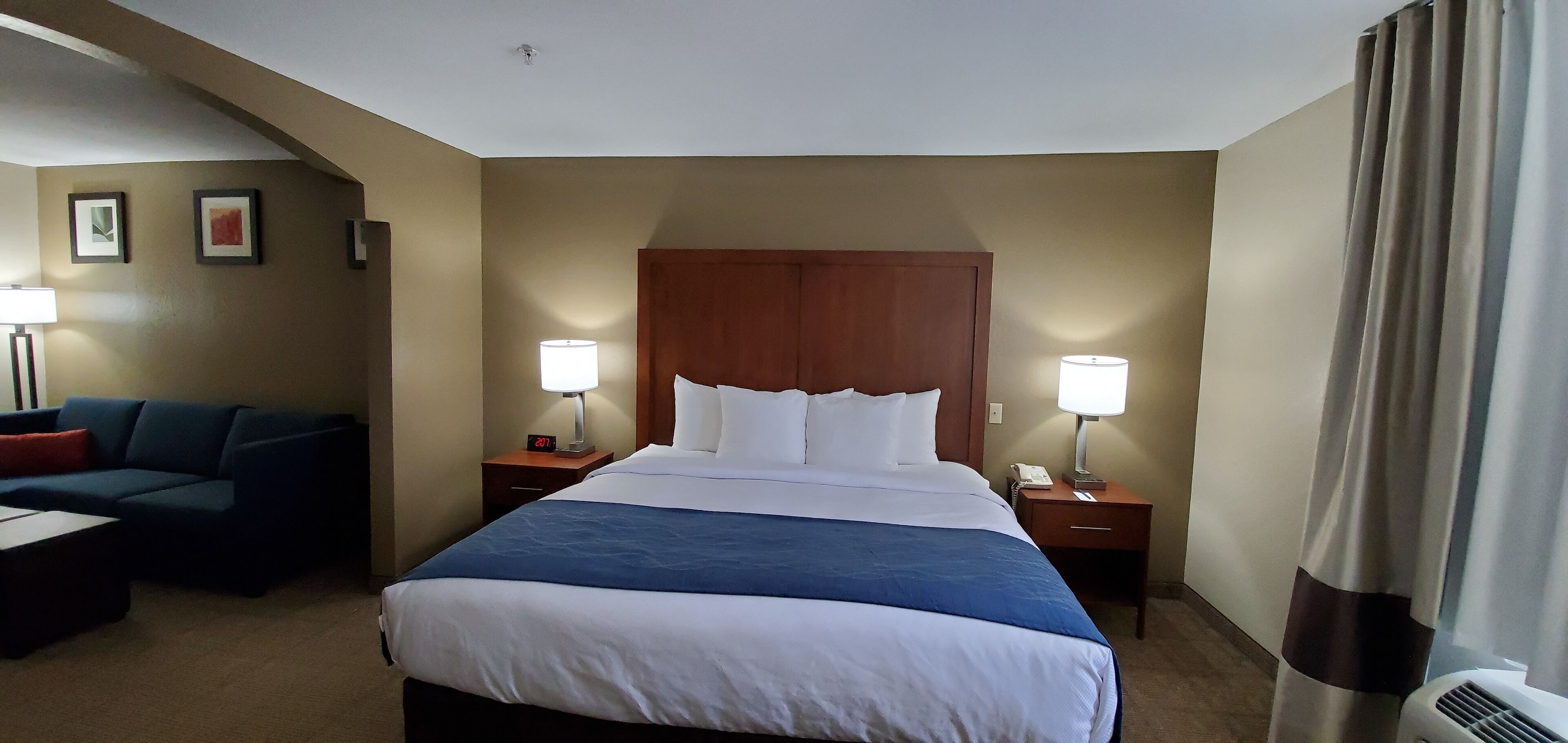Une chambre d’hôtel avec un grand lit, deux tables de chevet, une commode, un canapé et une lampe.
