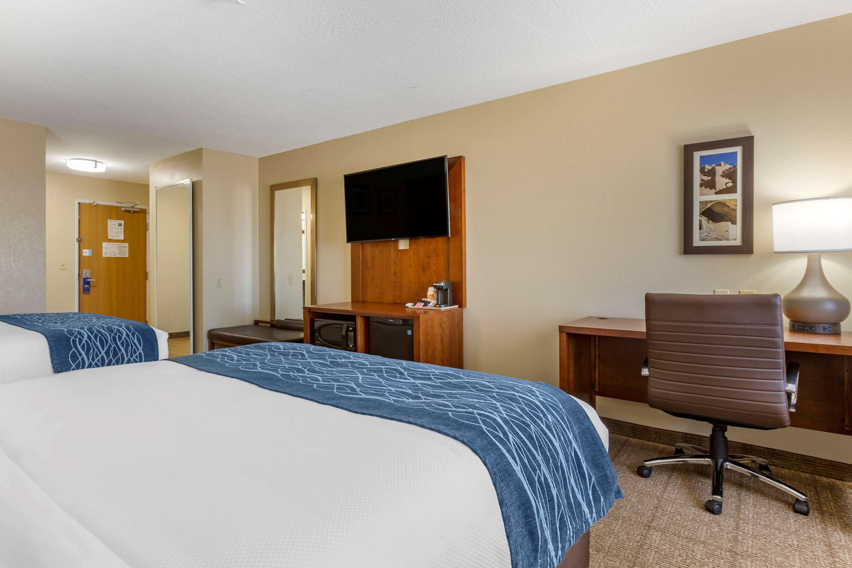 A hotel room with two beds, a desk, a chair, a TV, and a lamp.