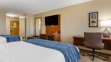 A hotel room with two beds, a desk, a chair, a TV, and a lamp.