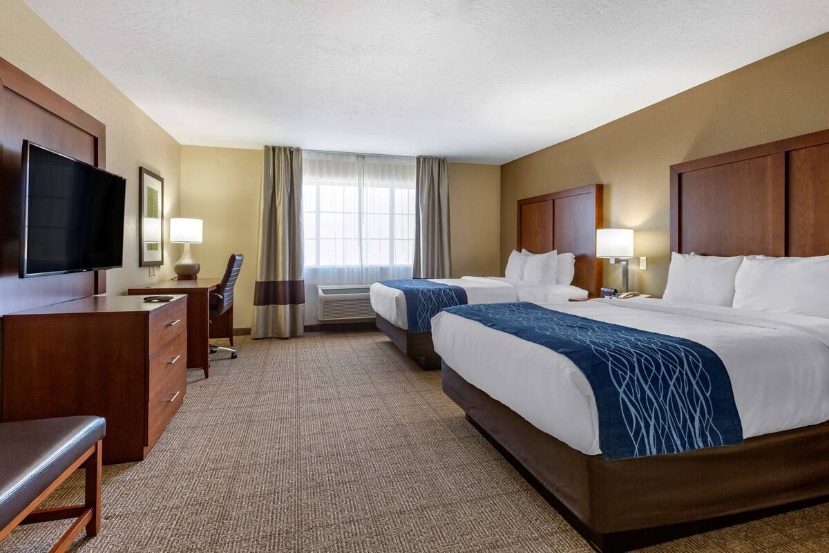 A hotel room with two beds, a desk, a chair, a TV, and a window with curtains.
