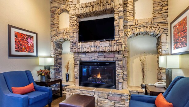 A living room with a stone fireplace, two blue armchairs, and a flat-screen TV mounted above the fireplace. - Comfort Inn & Suites Lordsburg I-10 (Lordsburg)