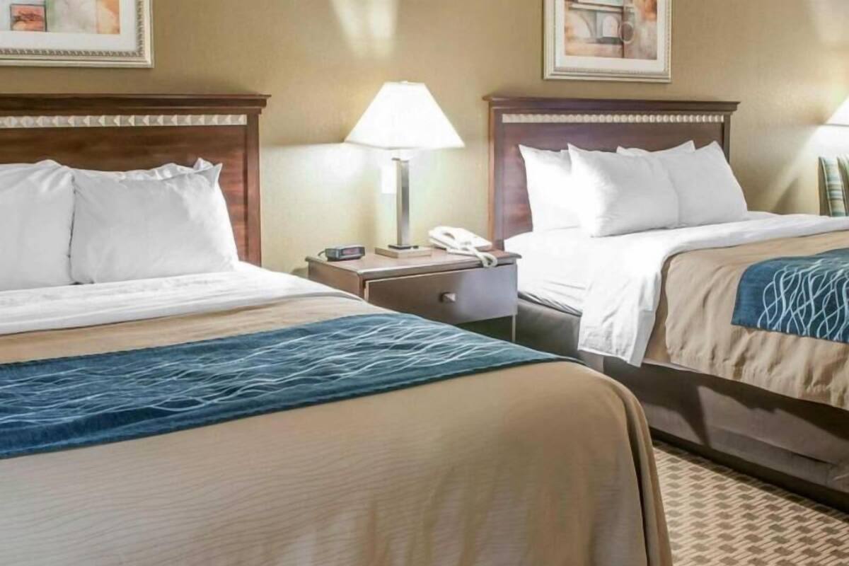 A hotel room with two beds, a nightstand with a lamp, and a telephone.