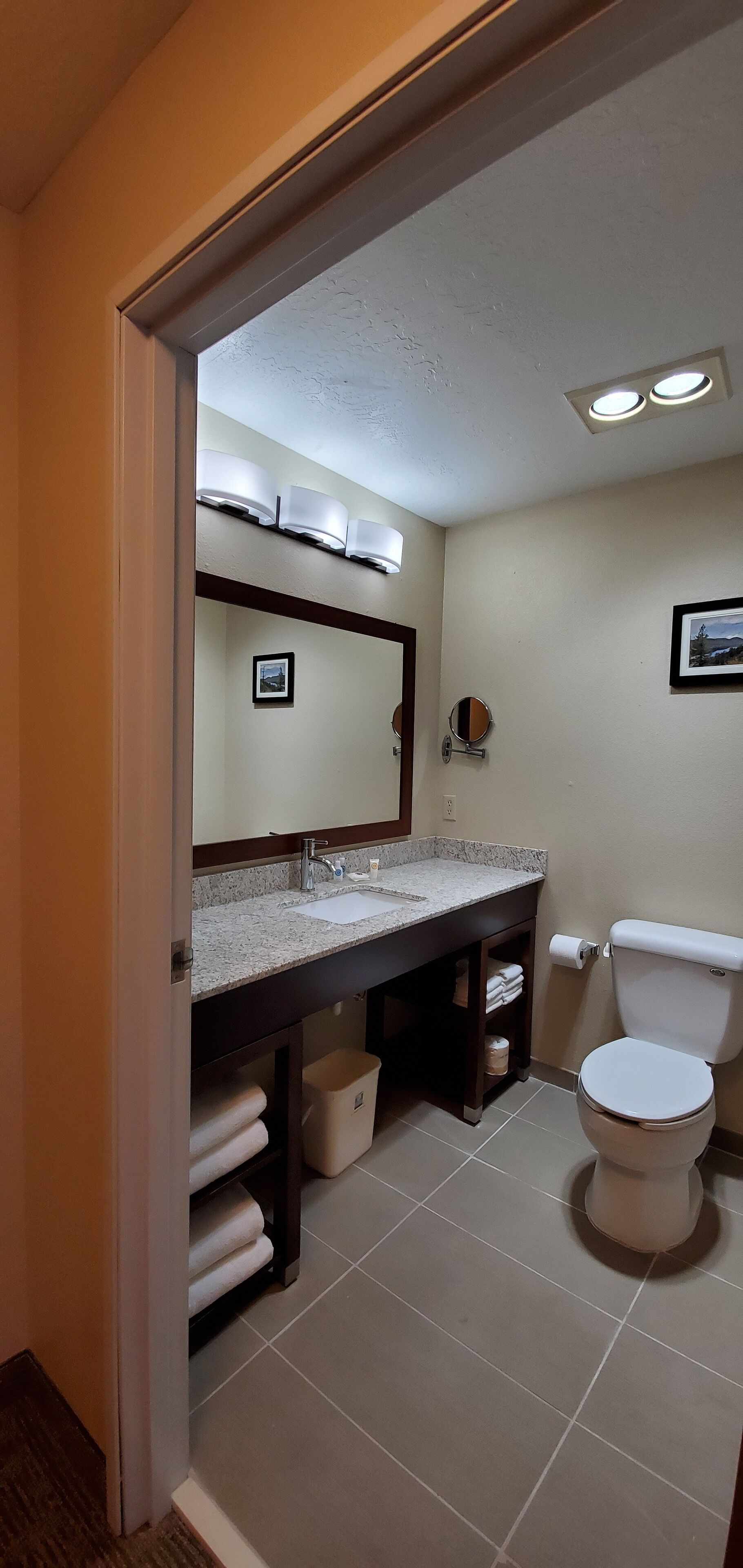 A bathroom with a sink, mirror, toilet, and towel storage.