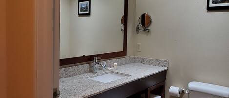 A bathroom with a sink, mirror, toilet, and towel storage.