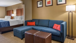 A hotel room with a bed, a blue sofa, a brown ottoman, and a floor lamp. - Comfort Inn & Suites Lordsburg I-10 (Lordsburg)
