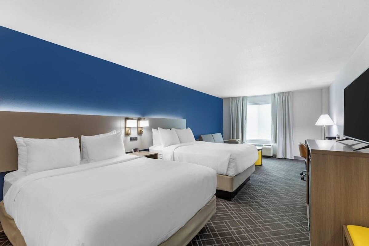 Una habitación de hotel con dos camas, un escritorio, una lámpara y una ventana con cortinas.