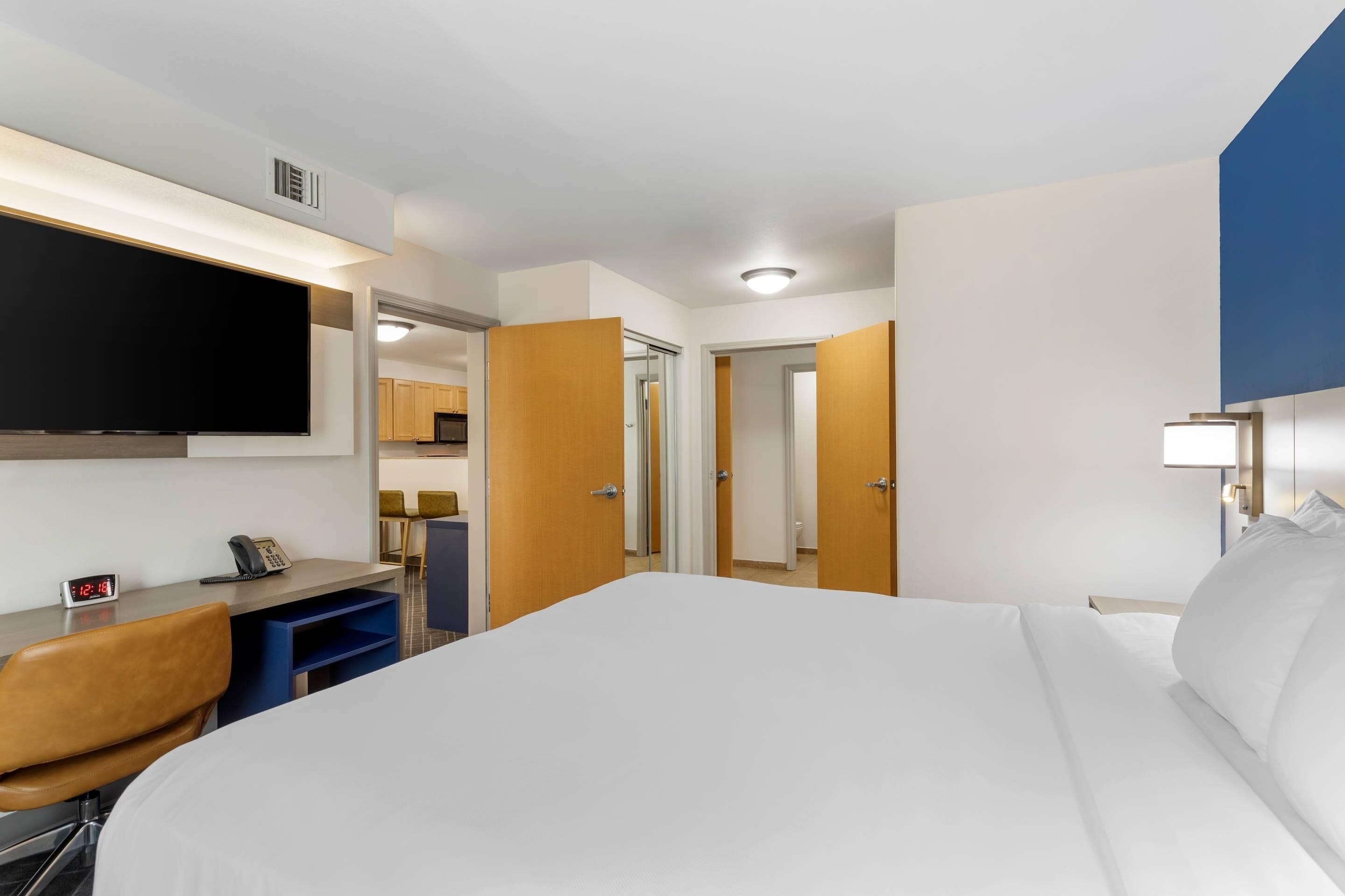 Habitación de hotel con cama, escritorio, silla, televisor y puerta que da a un baño.