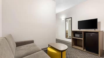 A modern hotel room with a sofa, a small yellow stool, a flat-screen TV, a microwave, and a refrigerator.