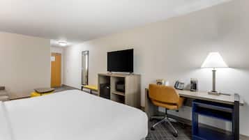 A hotel room with a bed, desk, chair, TV, lamp, and a small table with a coffee maker.