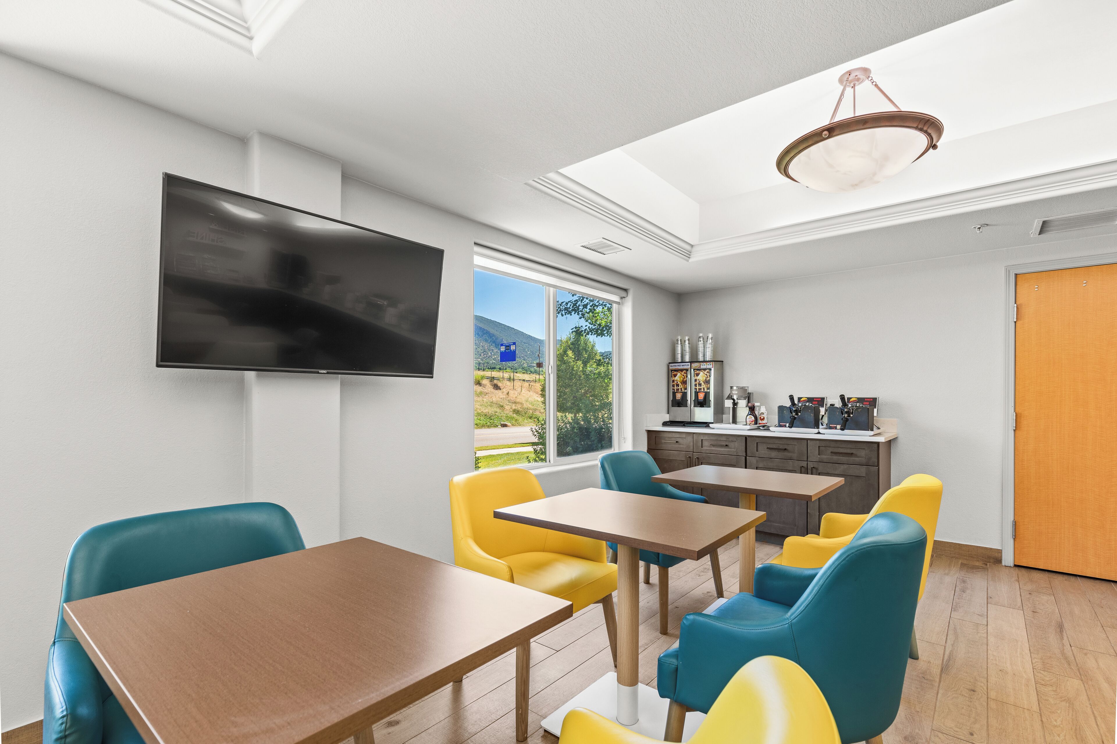 Un espace repas moderne doté d’un téléviseur à écran plat, de tables en bois et de chaises colorées.