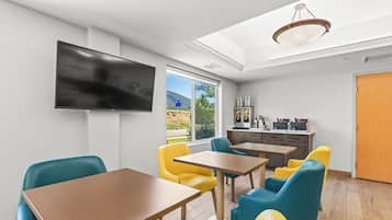 Un espace repas moderne doté d’un téléviseur à écran plat, de tables en bois et de chaises colorées.