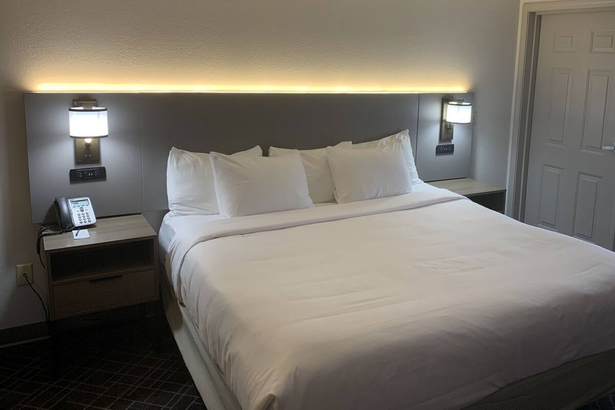 A hotel room with a large bed, two bedside tables with lamps, a phone, and a door.