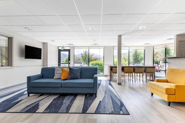 A modern hotel lobby with a sofa, armchair, dining area, and large windows offering a mountain view.