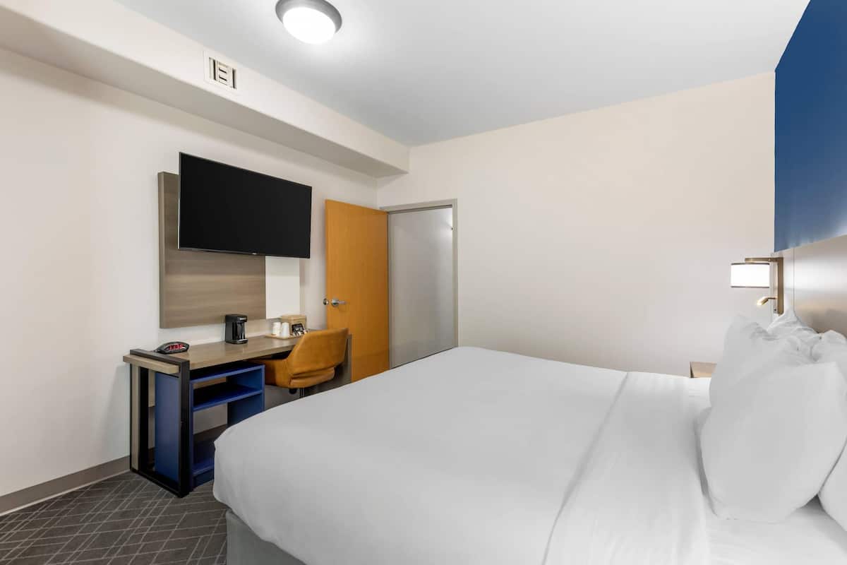 A hotel room with a bed, a desk with a chair, a television, and a door.