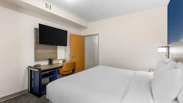 Une chambre d’hôtel avec un lit, un bureau et une chaise, une télévision et une porte.