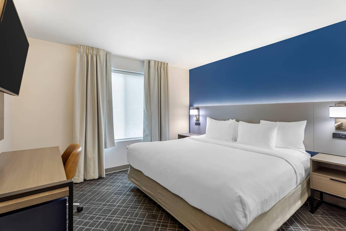 A hotel room with a large bed, a desk, a chair, a TV, and a window with curtains.