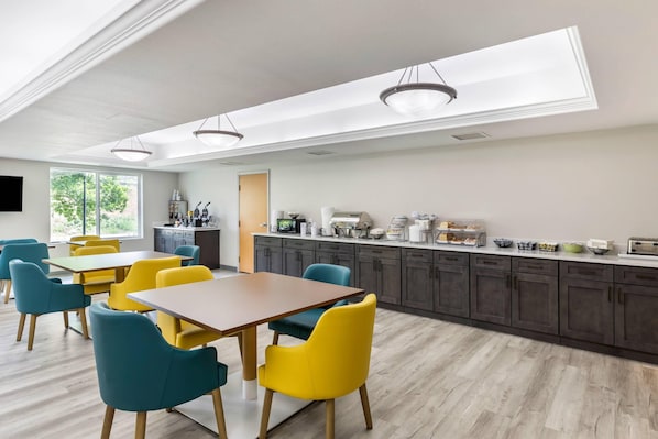 A modern dining area with a long table and chairs, a kitchen with dark cabinets, and a skylight above.