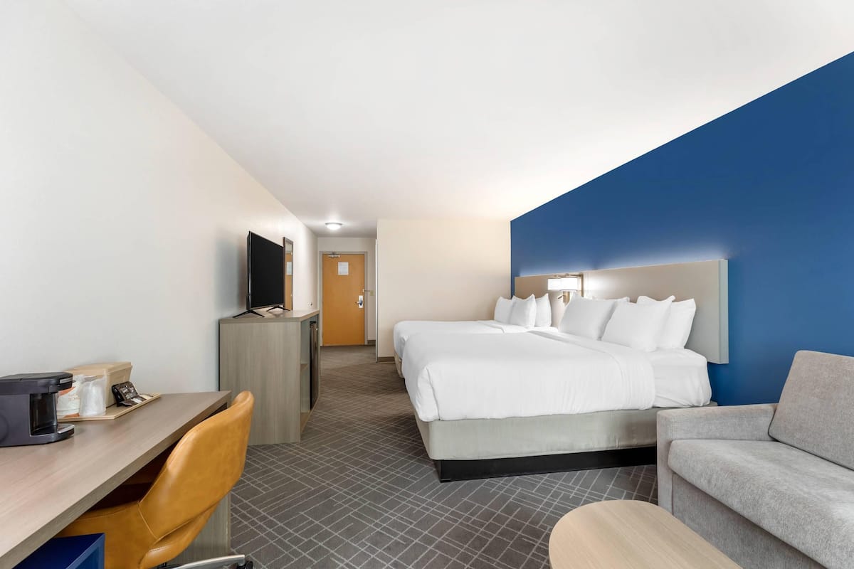 A hotel room with a bed, a desk with a computer, a chair, a sofa, and a television.
