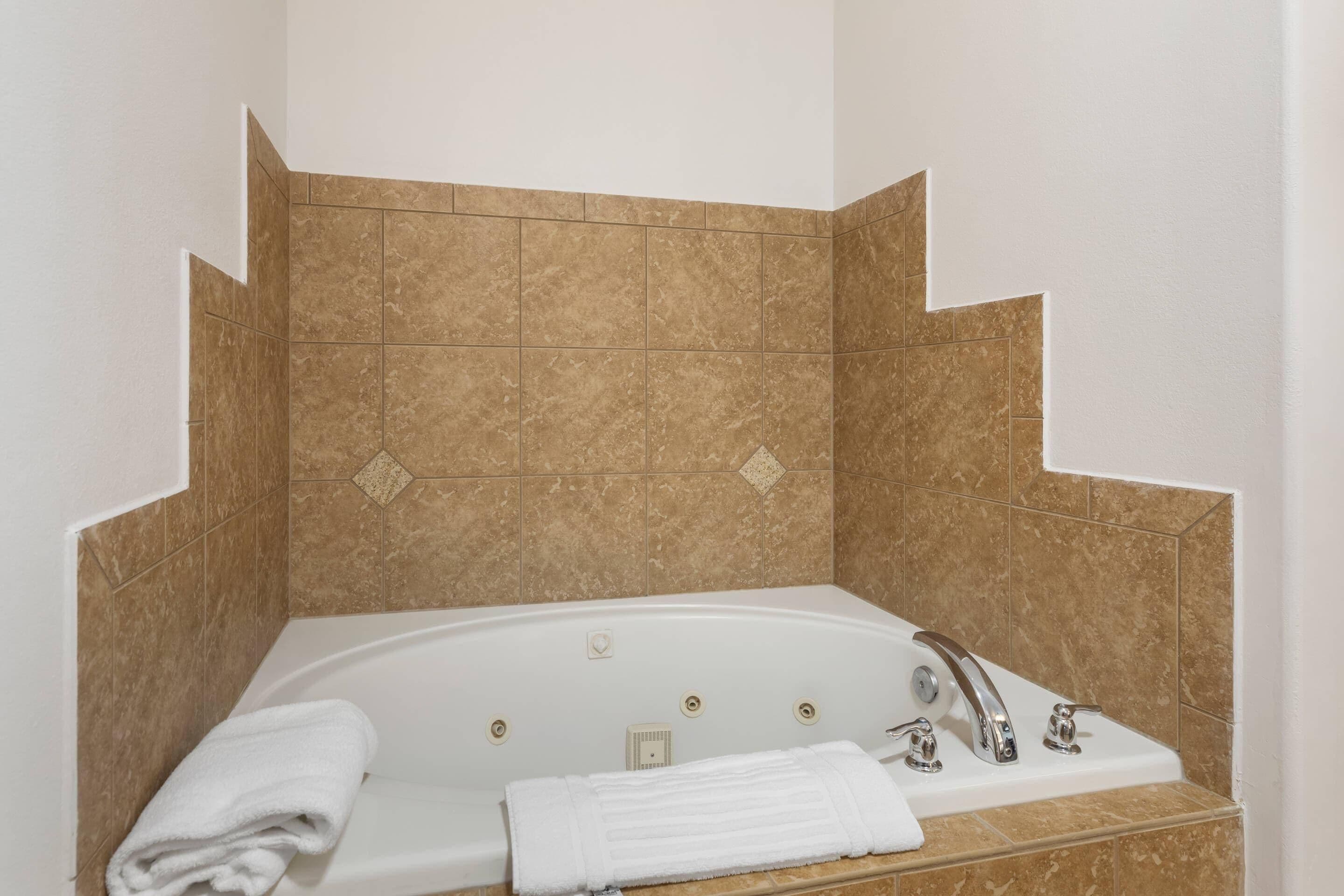 A bathroom with a bathtub, a white towel, and brown tiles.