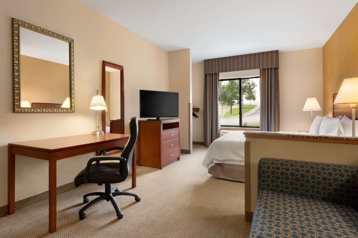A hotel room with a desk, chair, television, bed, and a view of the outdoors.