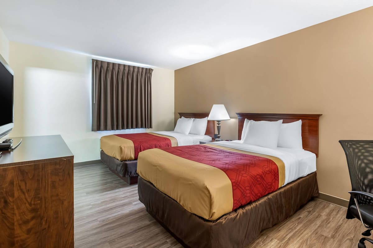 Habitación de hotel con dos camas, un escritorio, una silla y un televisor.