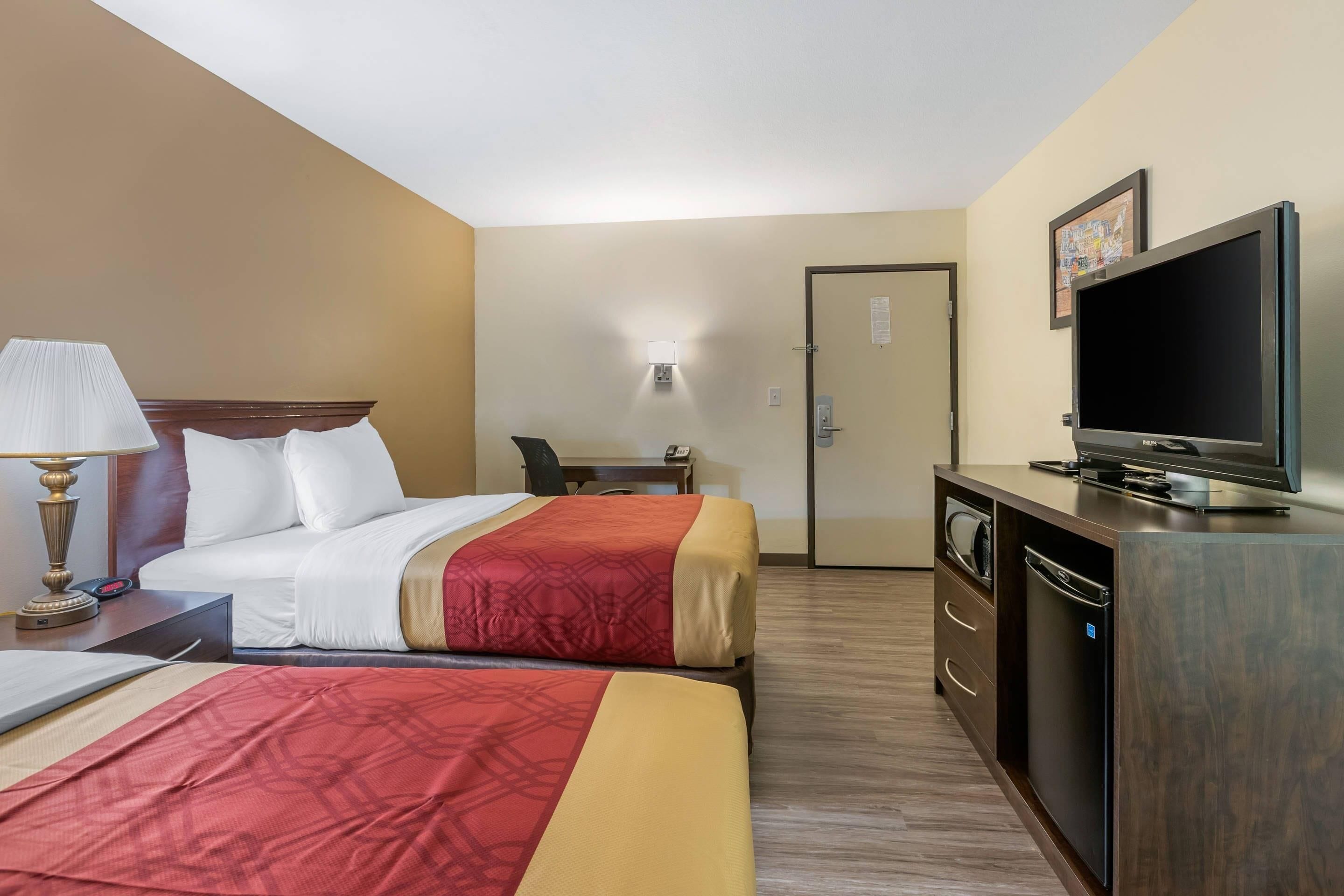 Une chambre d’hôtel avec deux lits, un bureau avec une lampe, une télévision et une armoire.