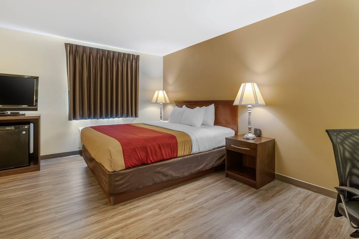 Una habitación de hotel con una cama, dos lámparas de noche, un televisor y un escritorio con lámpara.