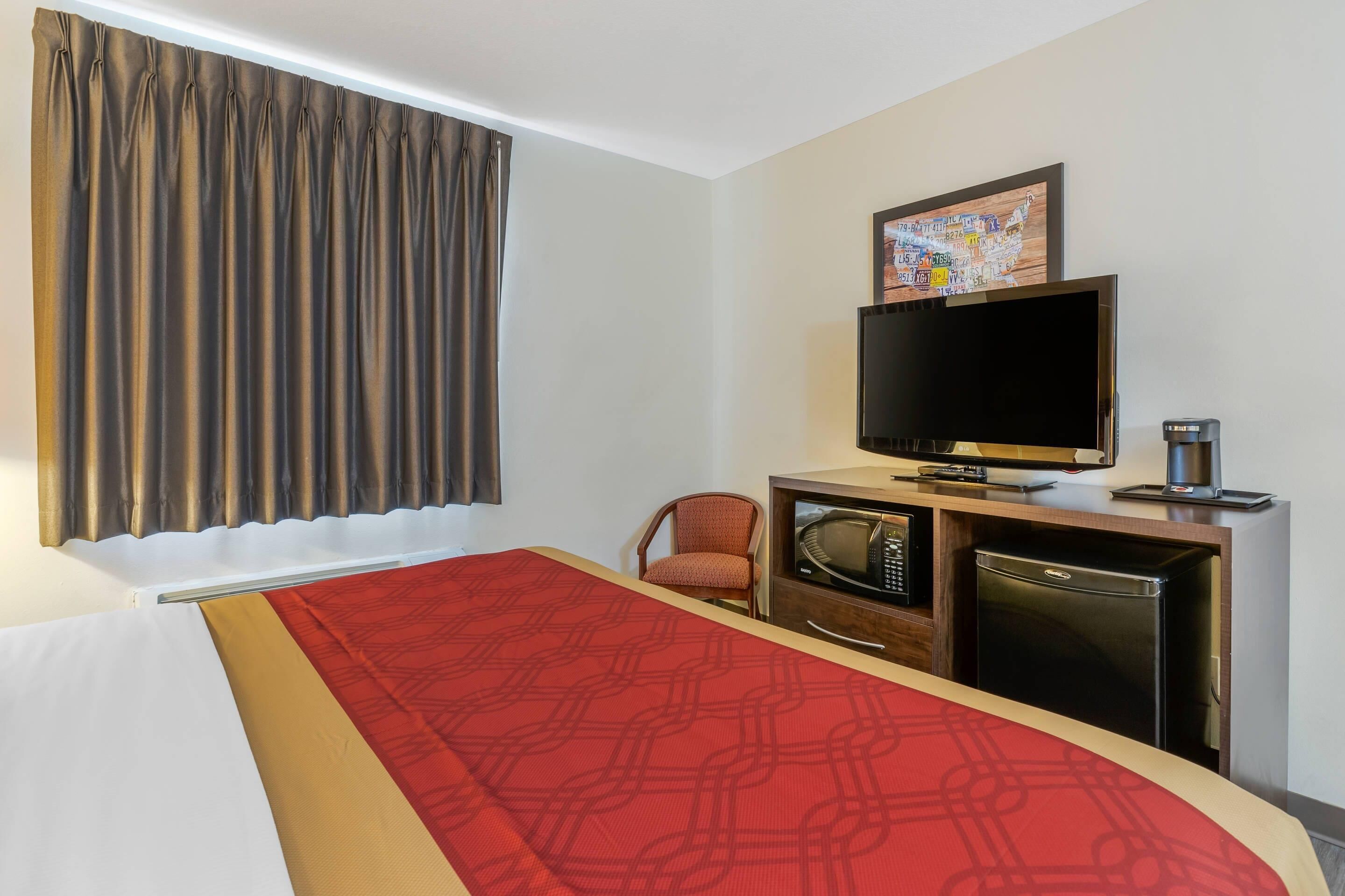 A hotel room with a bed, a television, a microwave, a refrigerator, and a chair.