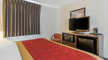 A hotel room with a bed, a television, a microwave, a refrigerator, and a chair.