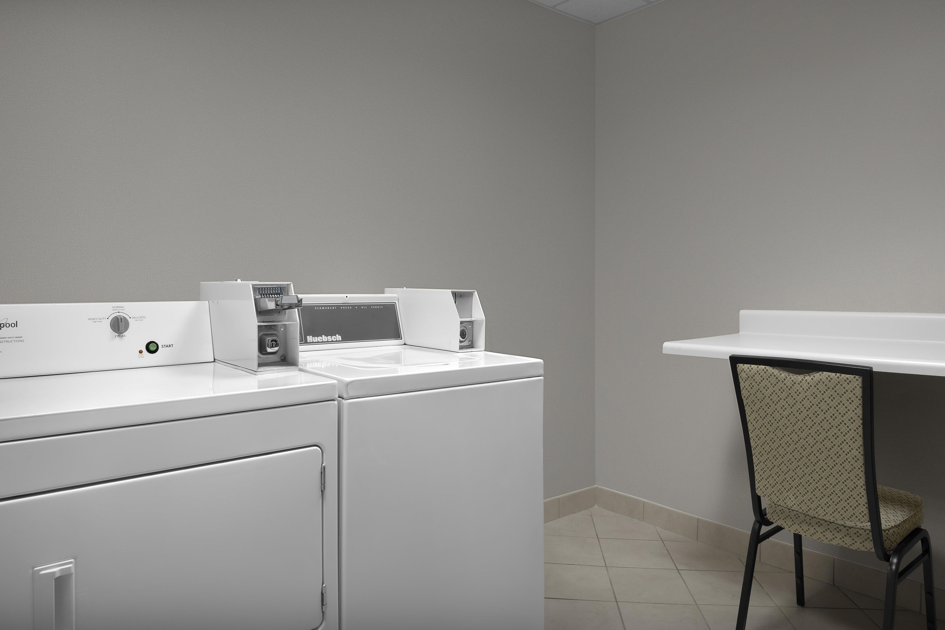 A laundry area with a washing machine, dryer, and a chair.