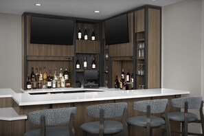 Zona de bar moderna con mostrador blanco, varias botellas de vino, un televisor de pantalla plana y taburetes de bar.