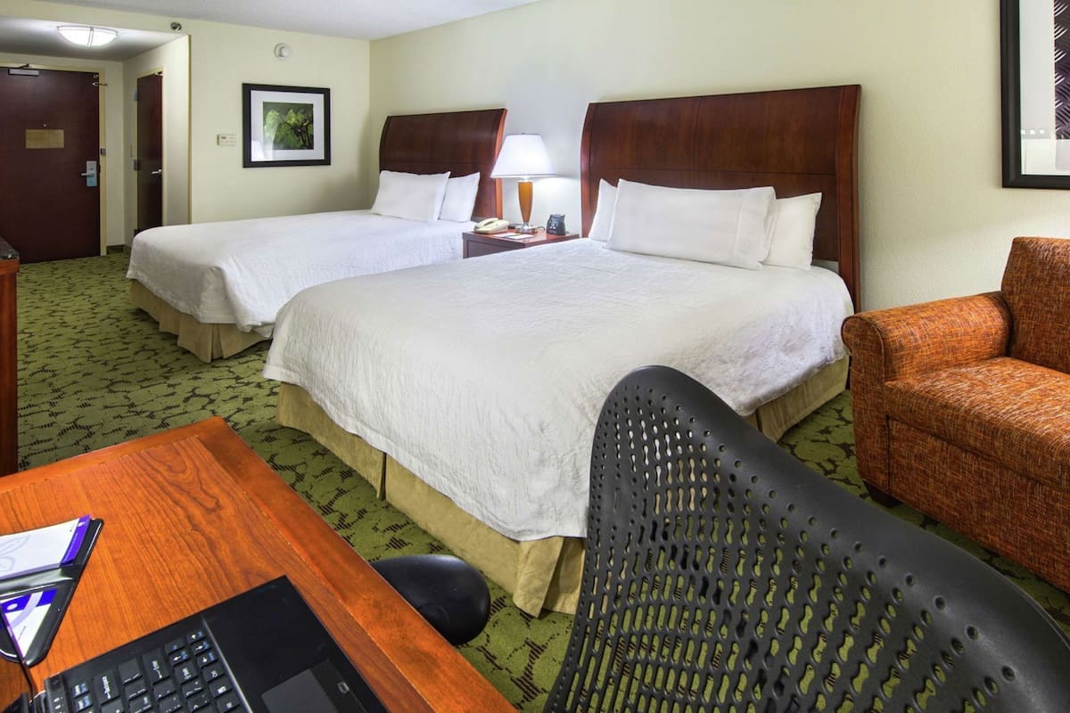 A hotel room with two beds, a desk with a computer, a chair, and a TV.