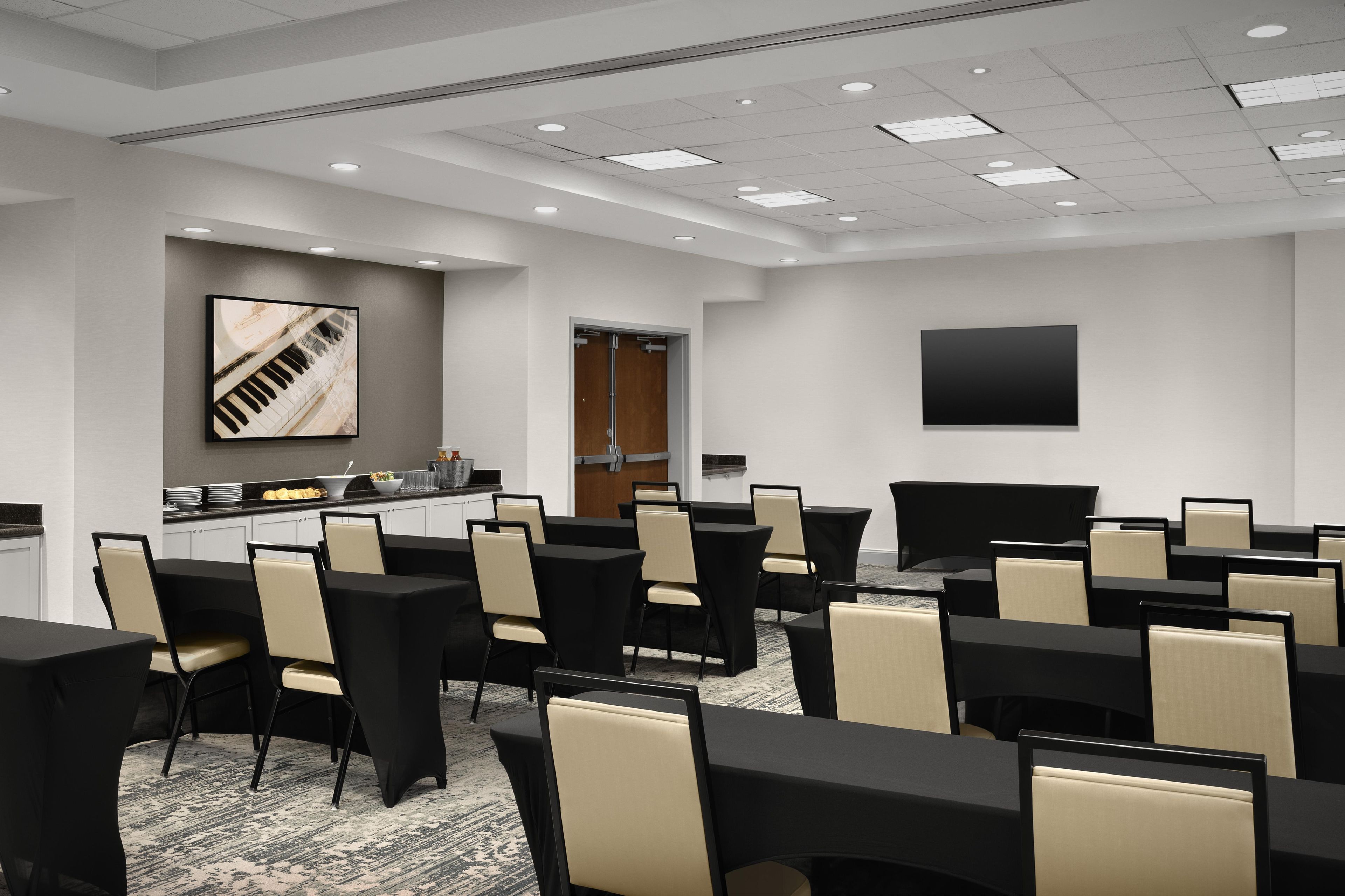 A conference room with multiple tables and chairs, a large painting on the wall, and a door leading to another room.