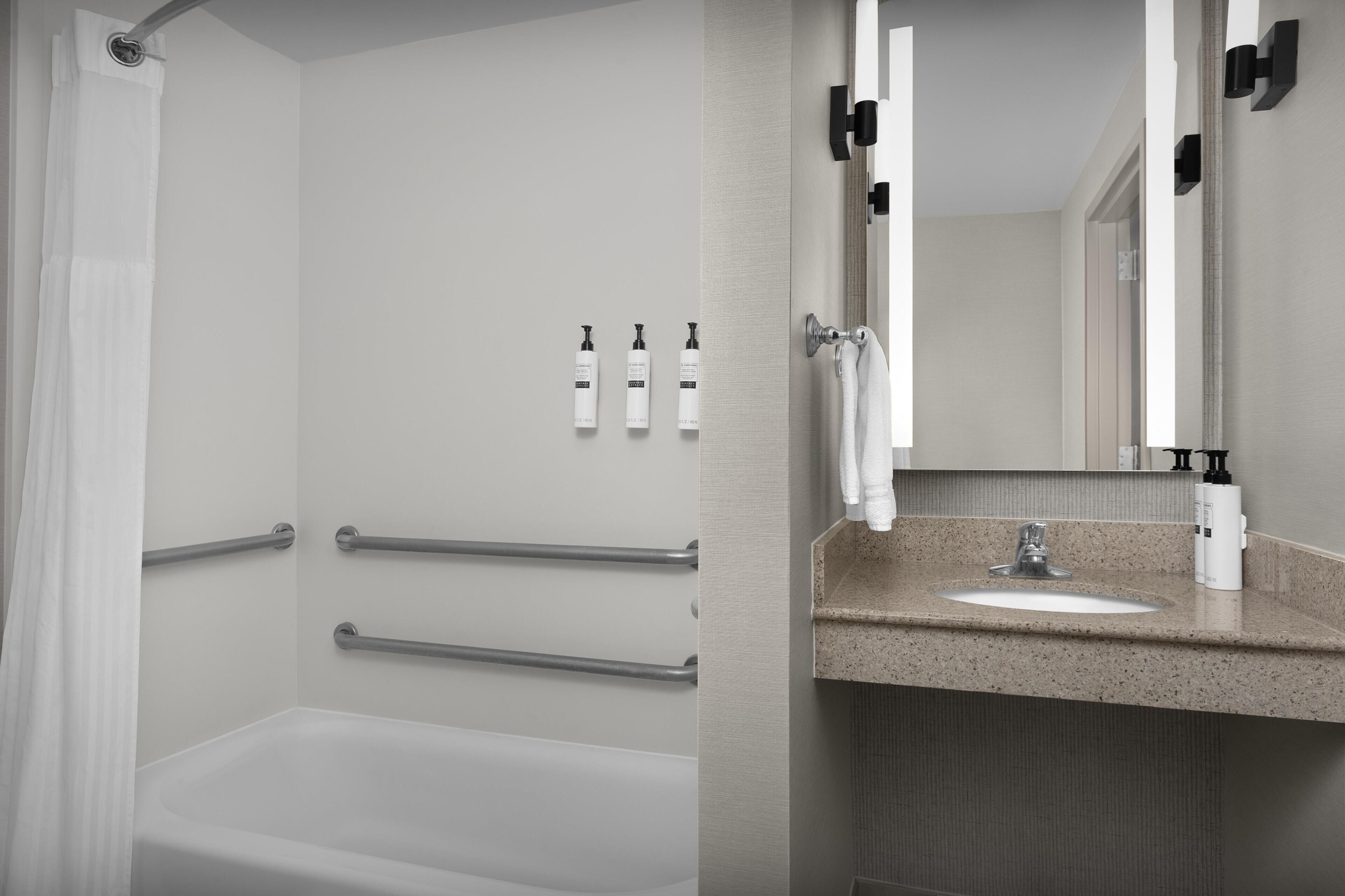 Un baño moderno con bañera, lavamanos con espejo y barras de apoyo.
