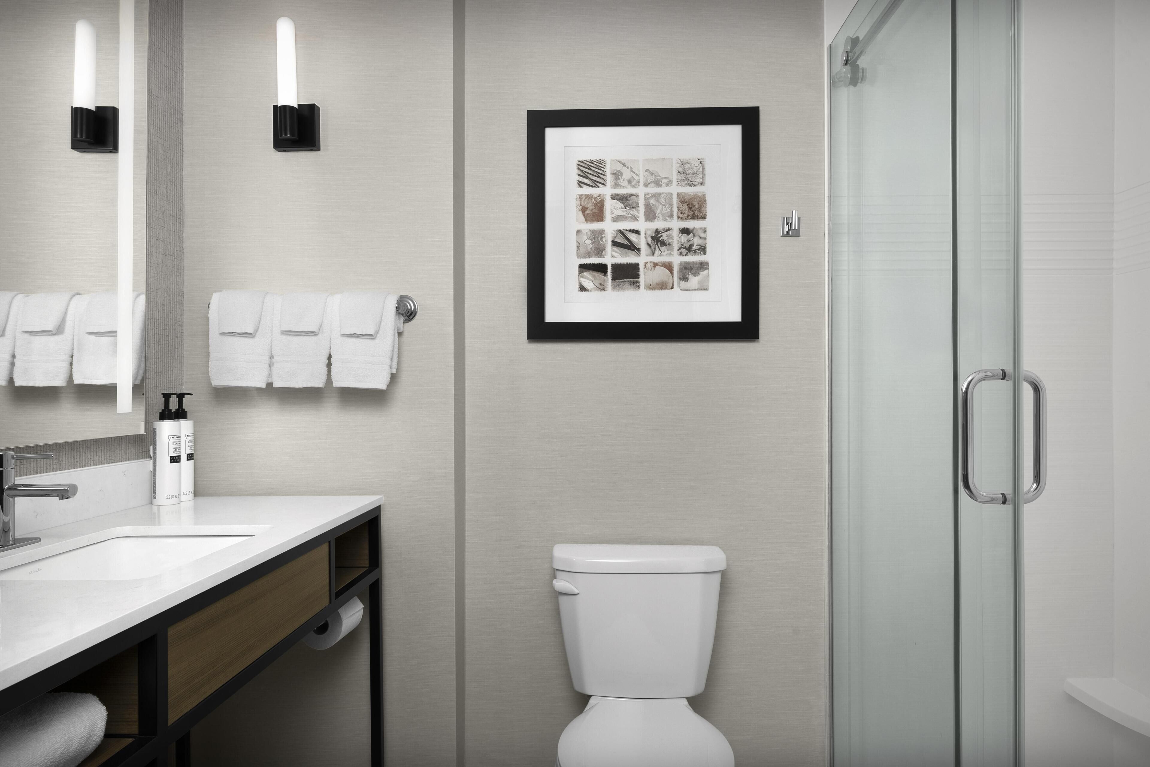 A modern bathroom with a sink, mirror, framed pictures, a toilet, and a shower.