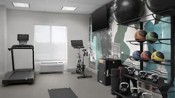 Une salle de sport équipée de matériel d’exercice, de tapis de course et d’un téléviseur fixé au mur.