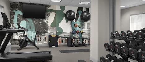 A gym with exercise equipment, including treadmills, weights, and a wall mural.