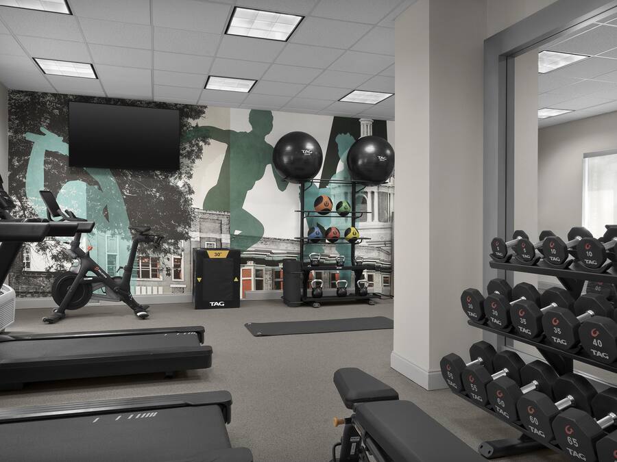 Un gimnasio con equipo de ejercicio, incluyendo cintas de correr, pesas y un mural.