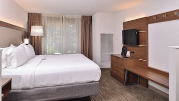Habitación de hotel con cama, escritorio, televisor y ventana con cortinas.