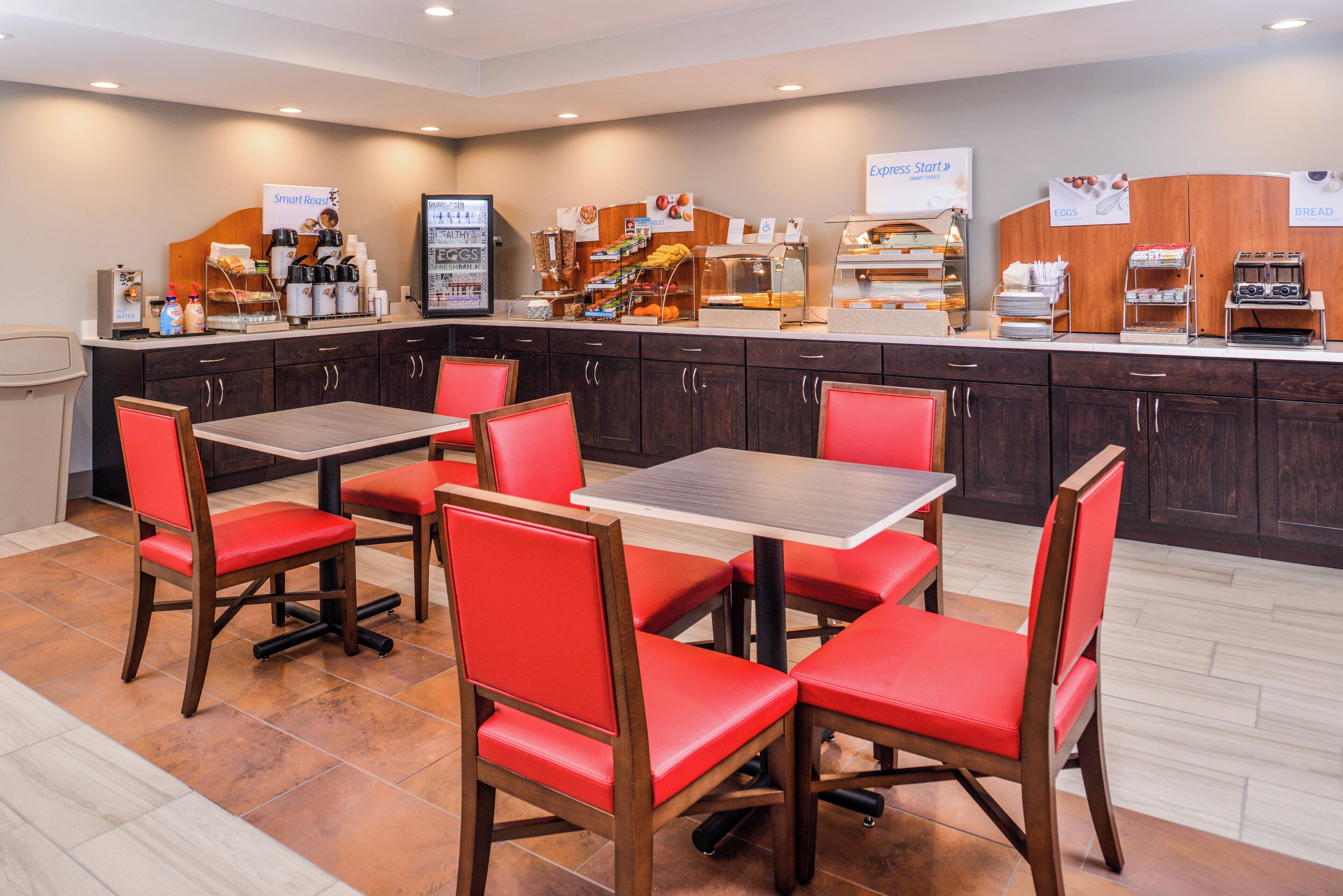 A hotel breakfast area with tables, chairs, and a variety of food and beverage options.