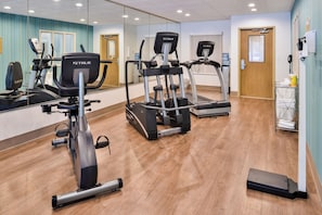 A fitness center with various exercise machines, including treadmills and an elliptical, and a mirror wall.
