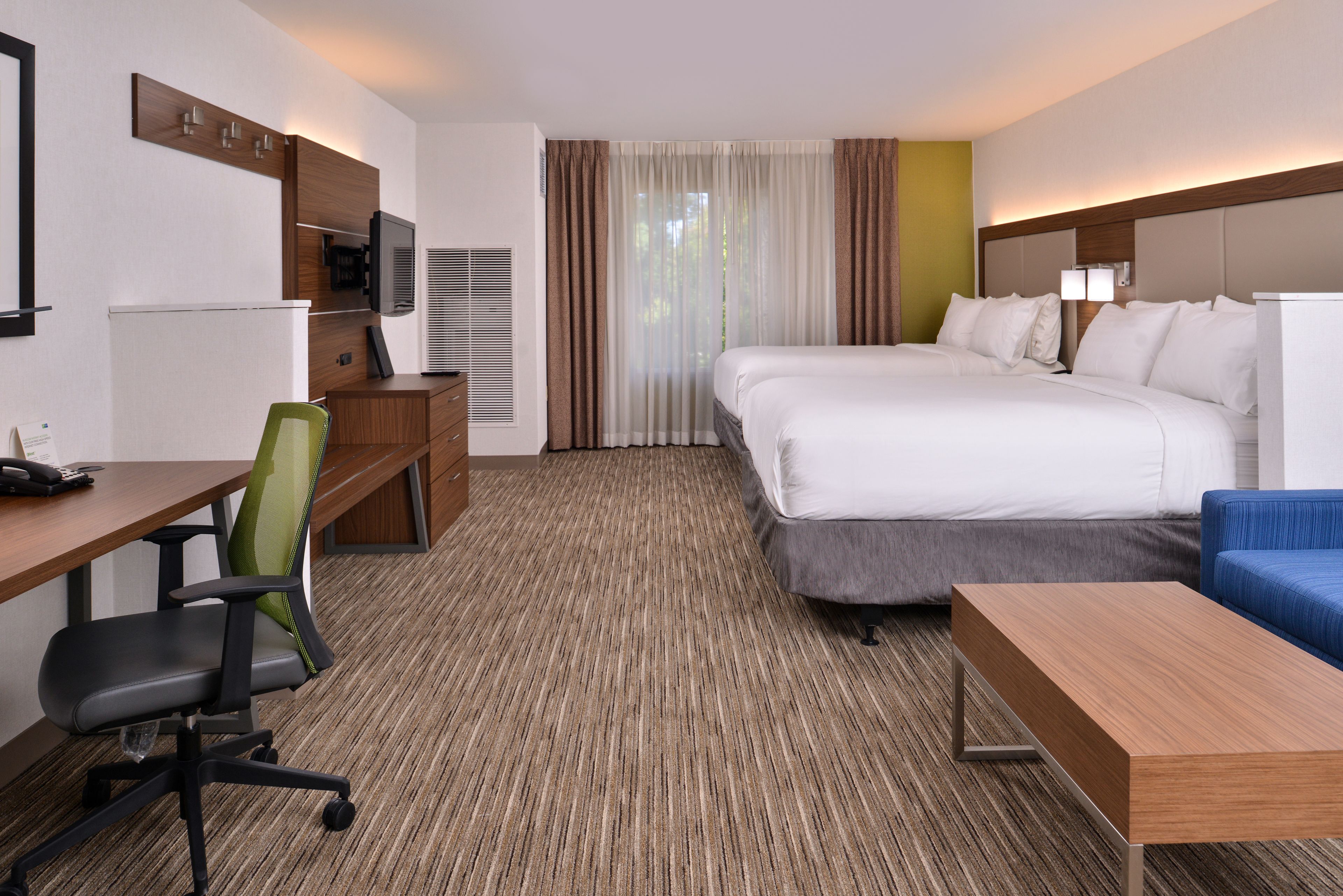 Ein Hotelzimmer mit einem Bett, einem Schreibtisch mit Stuhl, einem Fernseher und einem Fenster mit Vorhängen.