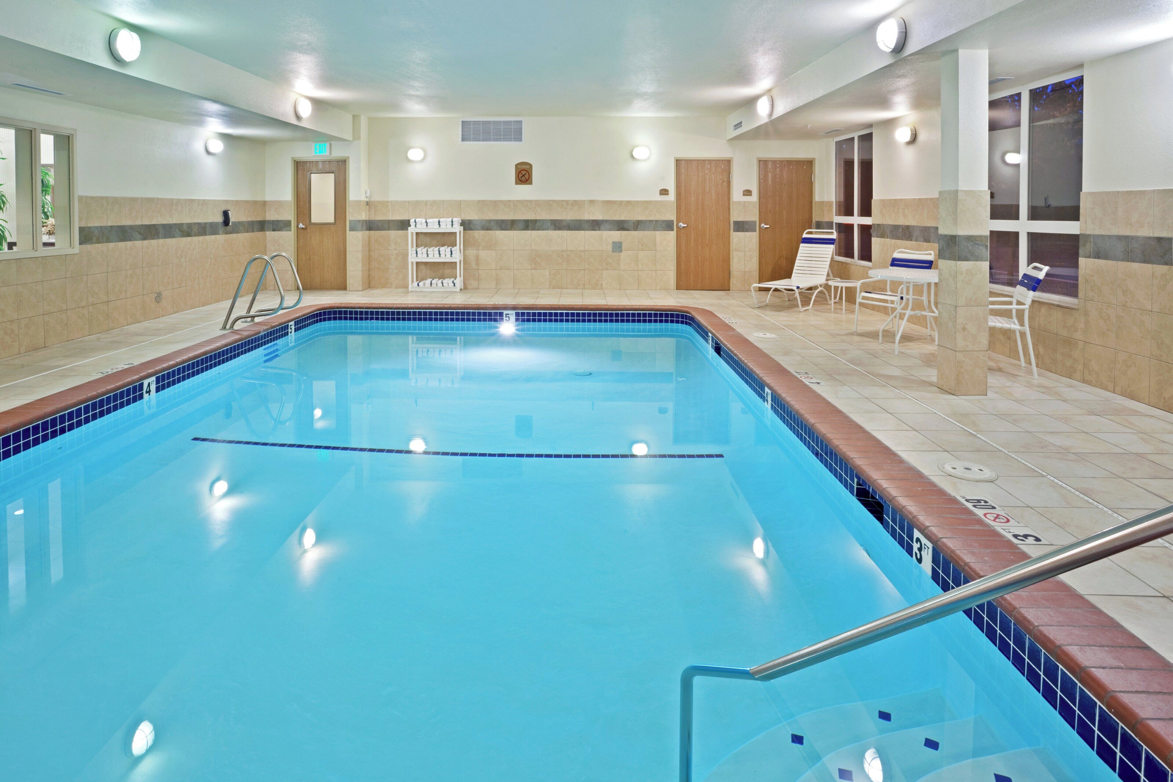 An indoor swimming pool with a tiled edge, a ladder, and lounge chairs.