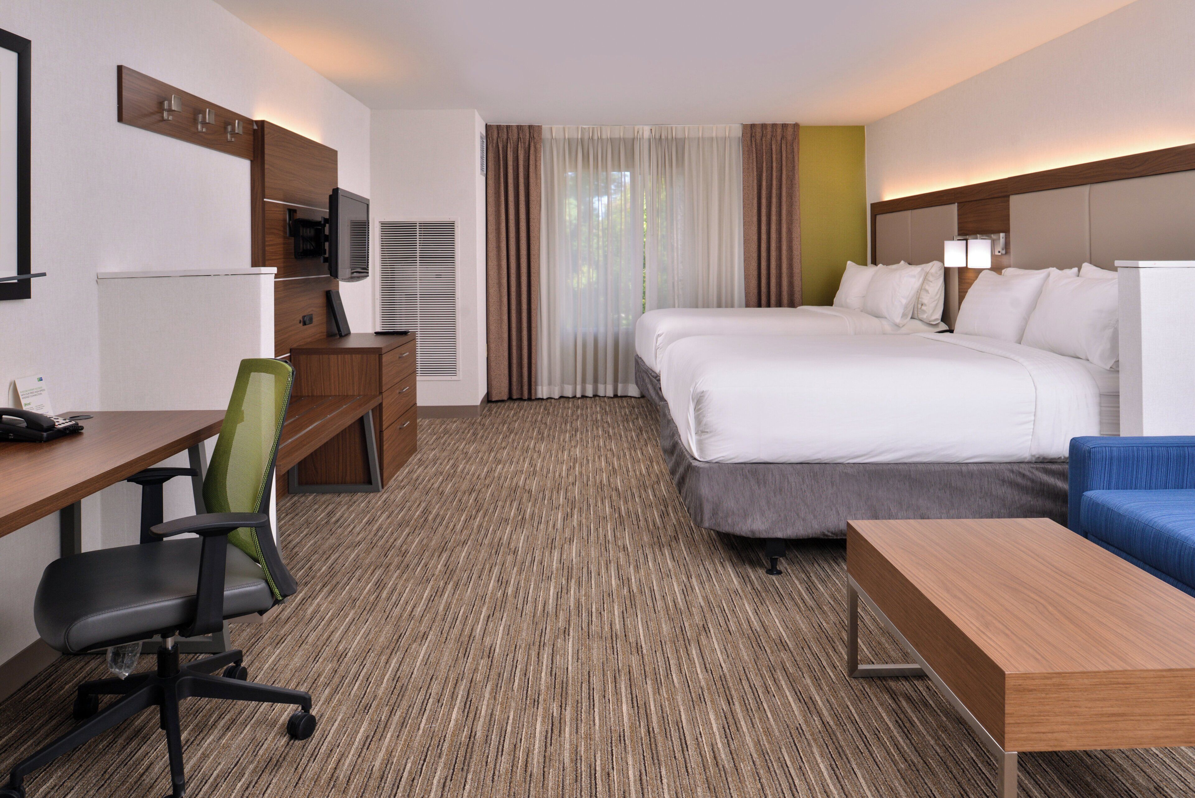 A hotel room with a bed, desk, chair, and a small table.