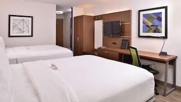 Habitación de hotel con dos camas, un escritorio con computadora, un televisor y obras de arte en las paredes.