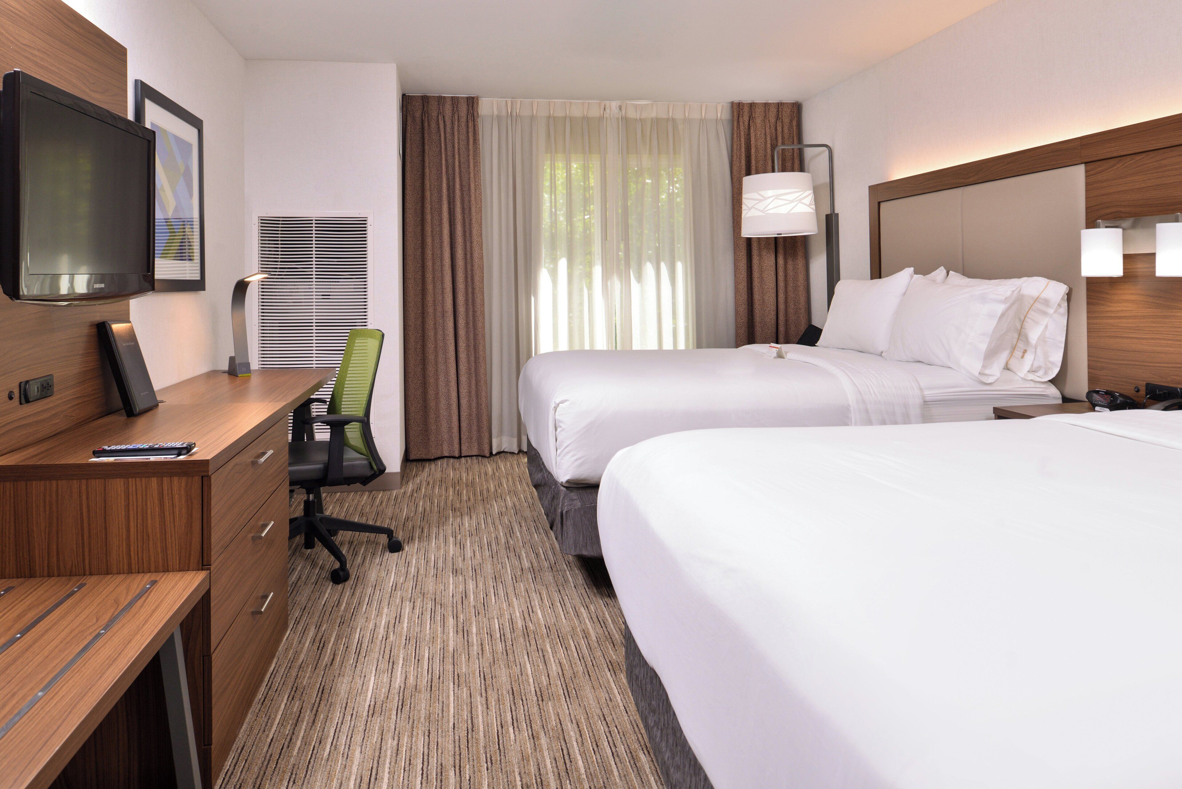 A hotel room with a bed, a desk, a chair, a television, and a window with curtains.