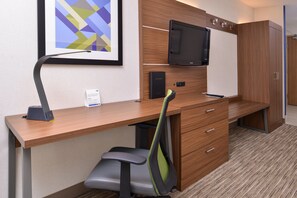 A hotel room with a wooden desk, a chair, a television, and a wardrobe.