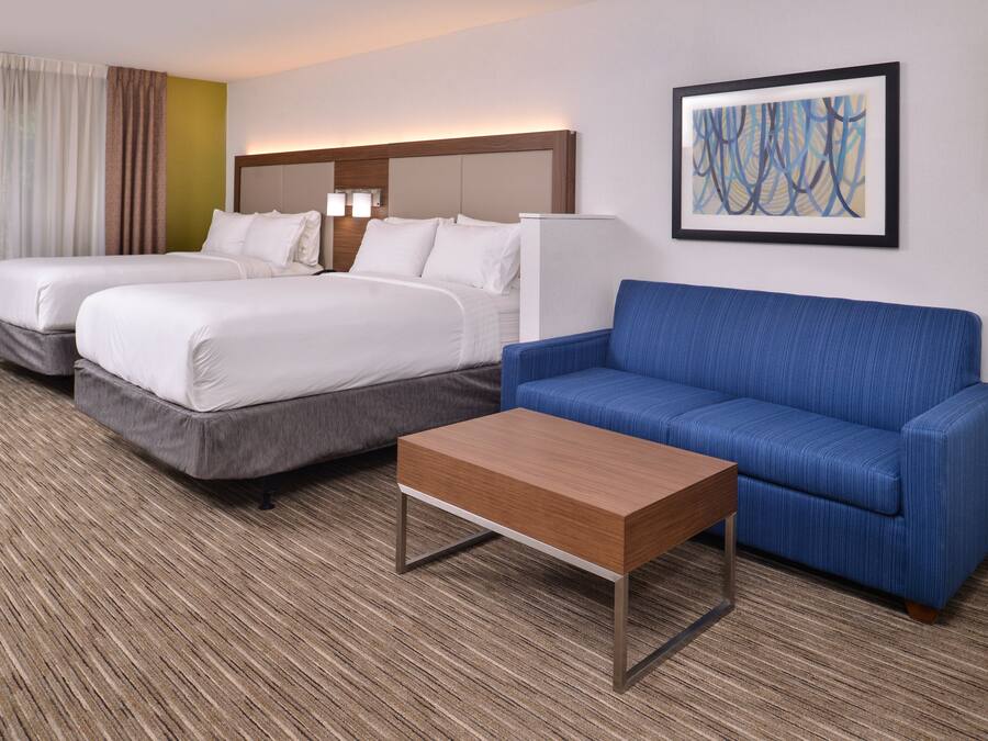 Una habitación de hotel con dos camas, un sofá azul y una mesa de centro de madera.