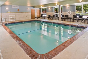 Una piscina con borde de azulejos, zona de vestuarios y área de estar con sillas y mesas.