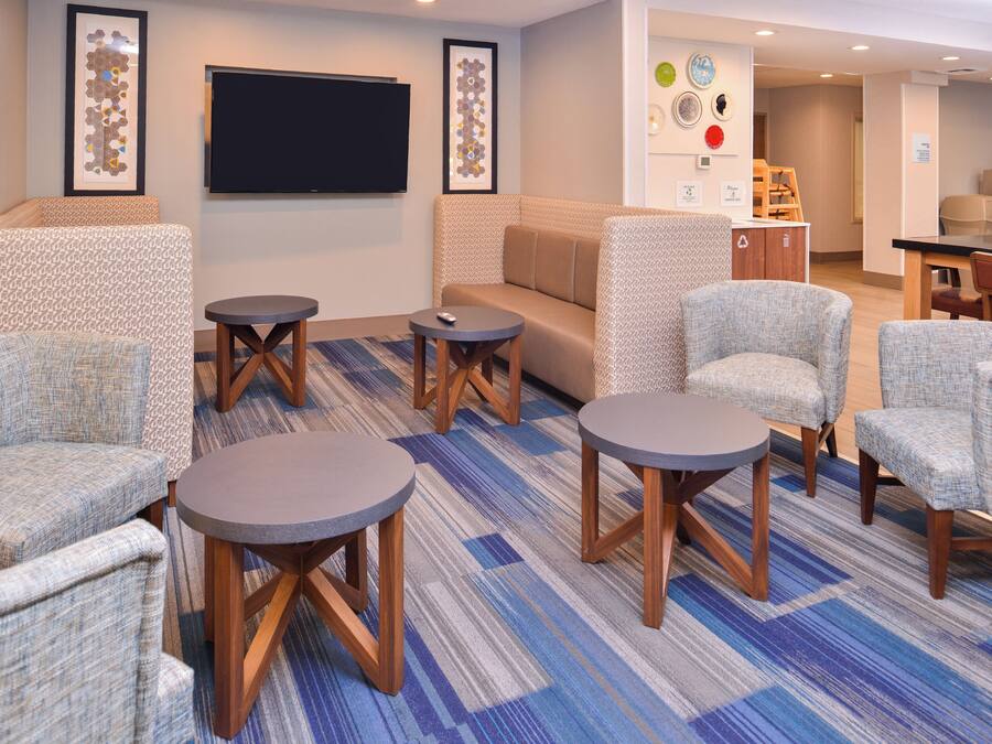 A hotel room with a sofa, armchairs, a coffee table, a flat-screen TV, and a carpeted floor.